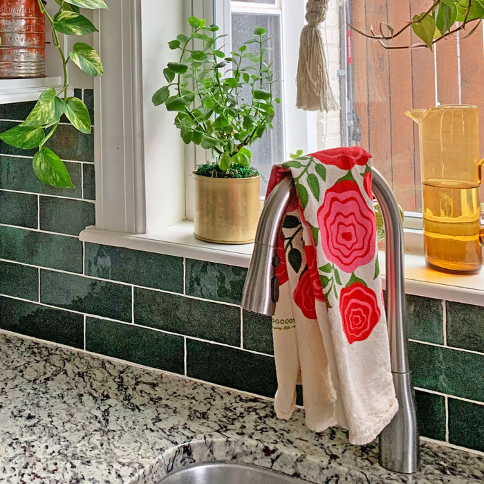 The Neighborgoods Roses dish towel hanging over kitchen sink faucet displaying rose flowers illustration.