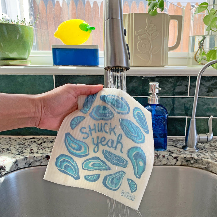 A oyster sponge cloth becomes wet under the running kitchen sink faucet.