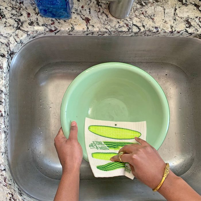 A woman washes a bowl  in the kitchen sink with a pickle sponge cloth.