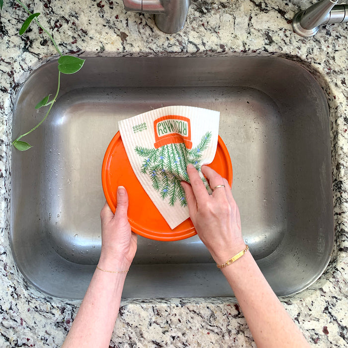 A woman washes a plate with a rosemary sponge cloth.