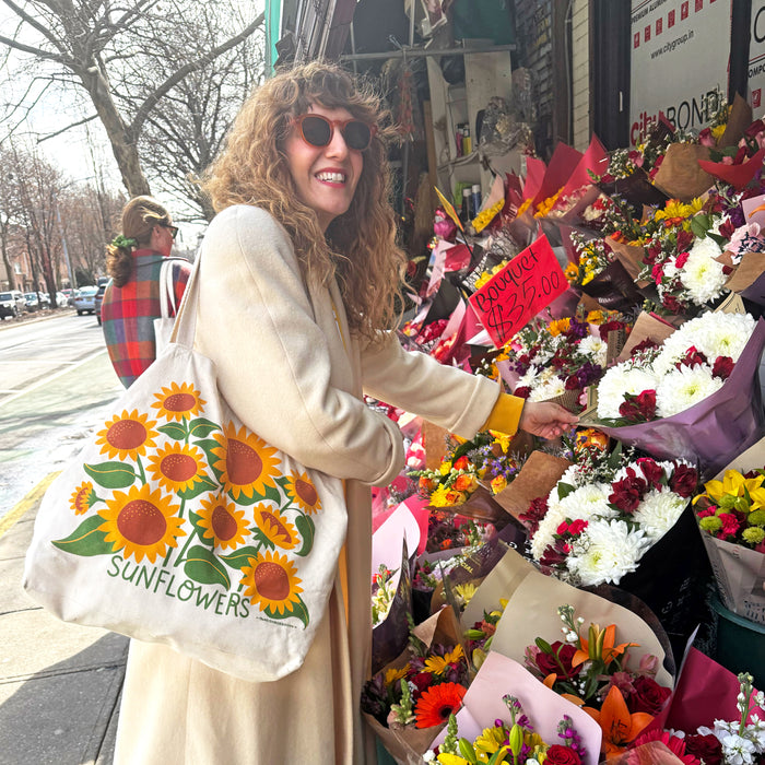 A woman at a flower stand with The Neighborgoods Sunflowers tote bag on her shoulder.