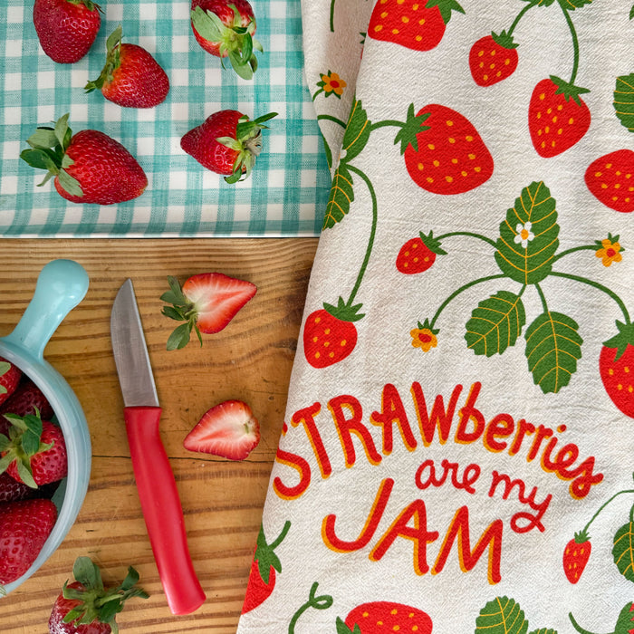 Strawberry kitchen dish towel laying on counter next to freshly cut strawberries.