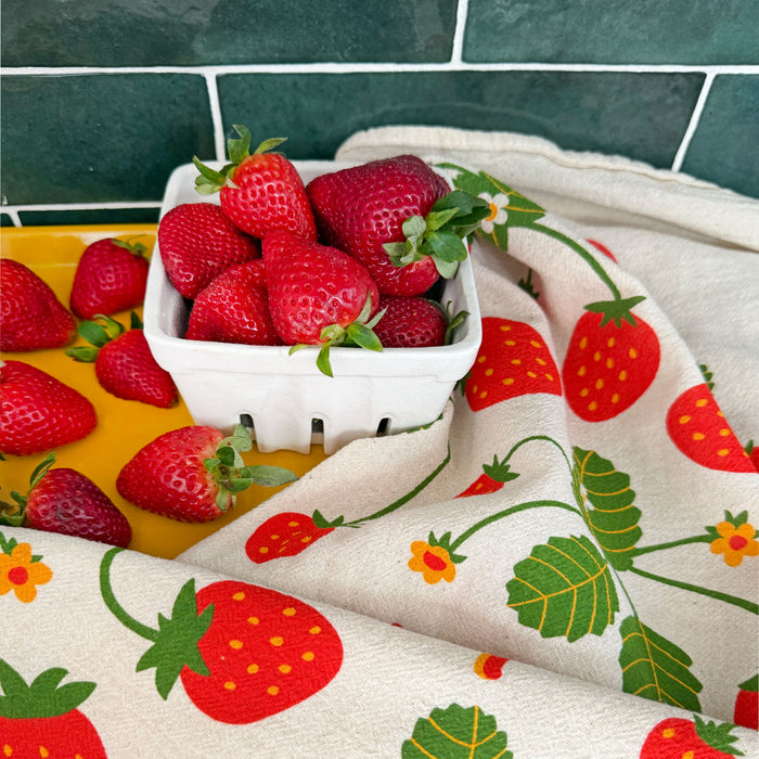 Strawberry kitchen tea towel alongside a produce carton contained with fresh strawberries.