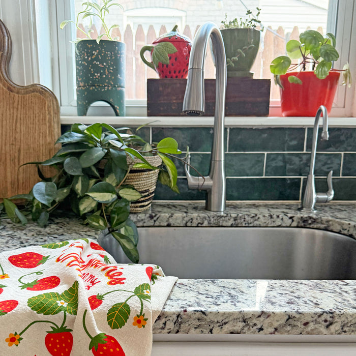 Strawberry tea towel draped over kitchen sink countertop ledge.