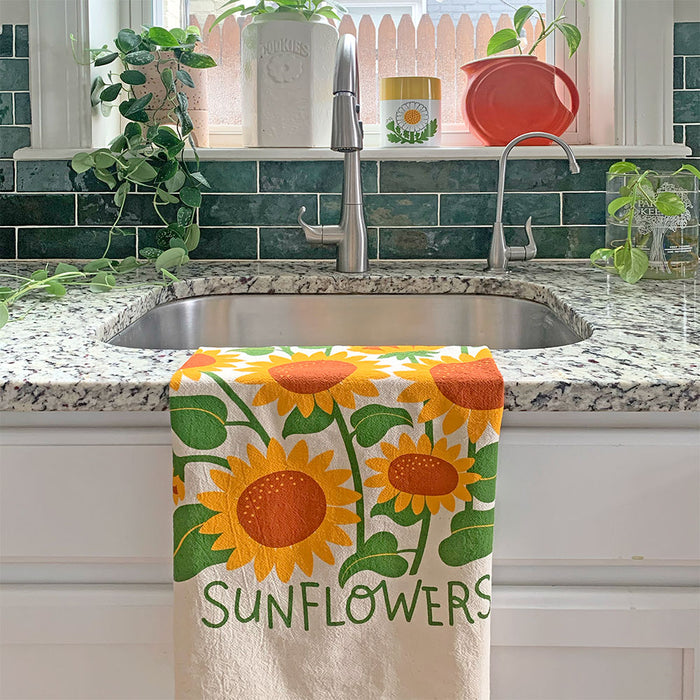 The Neighborgoods Sunflowers dish towel with a sunflower illustration draped over a kitchen countertop.