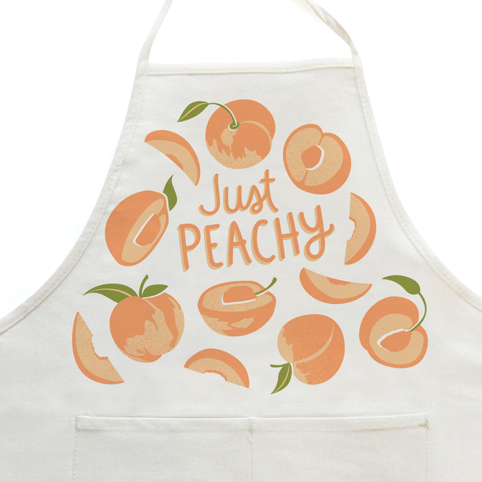 Close-up on white apron with peaches design, featuring the phrase "Just peachy"