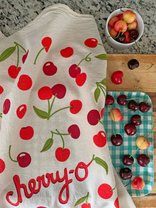 Cherry dish towel on a kitchen counter and cutting board with cherries