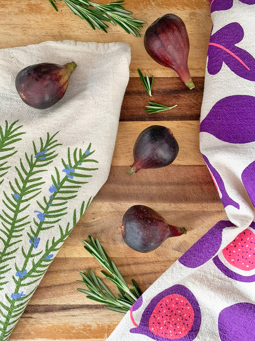 Rosemary  and Git Figgy With It dish towels draped on cutting board next to rosemary shrubs and figs