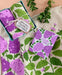 "I Lilac Purple" dish towel set photographed with folded lilac and mint dish towels, alongside Neighborgoods "I Lilac You" card and some small leafy branches