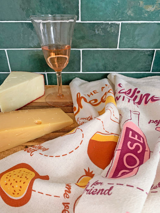Screen-printed cheese and wine dish towels on cutting board with blocks of cheese and glass of wine