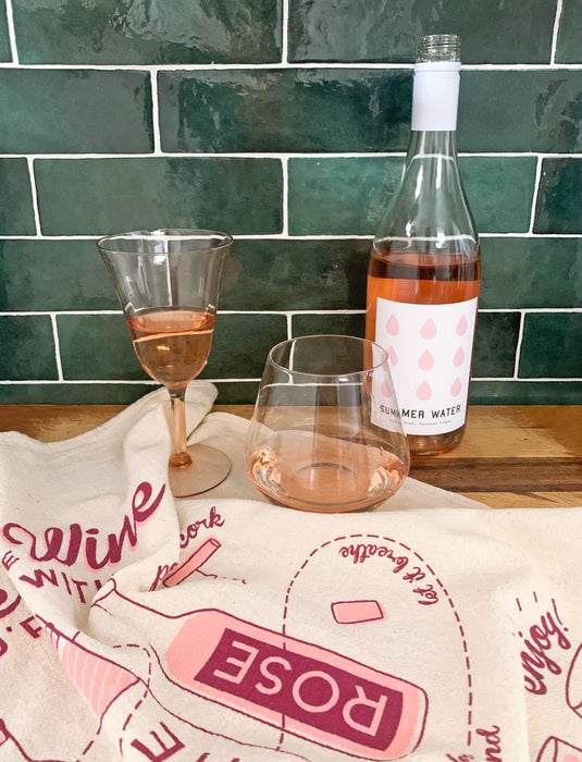 Wine dish towel pictured next to a bottle of wine and glasses.