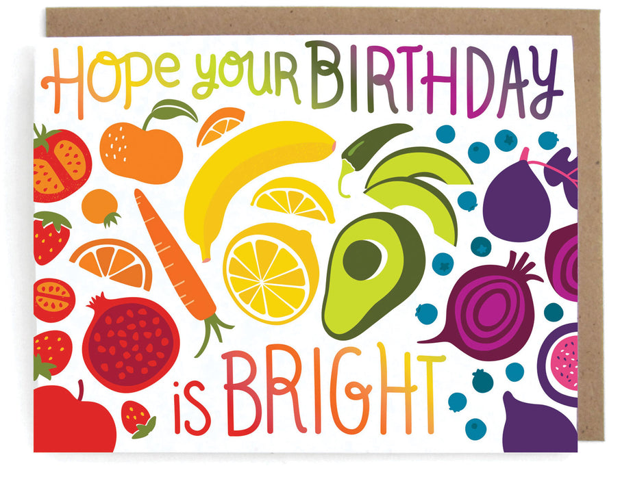 White card that pictures a rainbow of fruit and veggie designs, featuring the phrase "Hope your birthday is bright," with a brown envelope