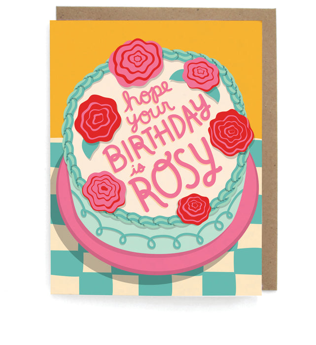 Card that pictures a rose decorated cake on a checkboard table, featuring the phrase "Hope your birthday is rosy," with a brown envelope