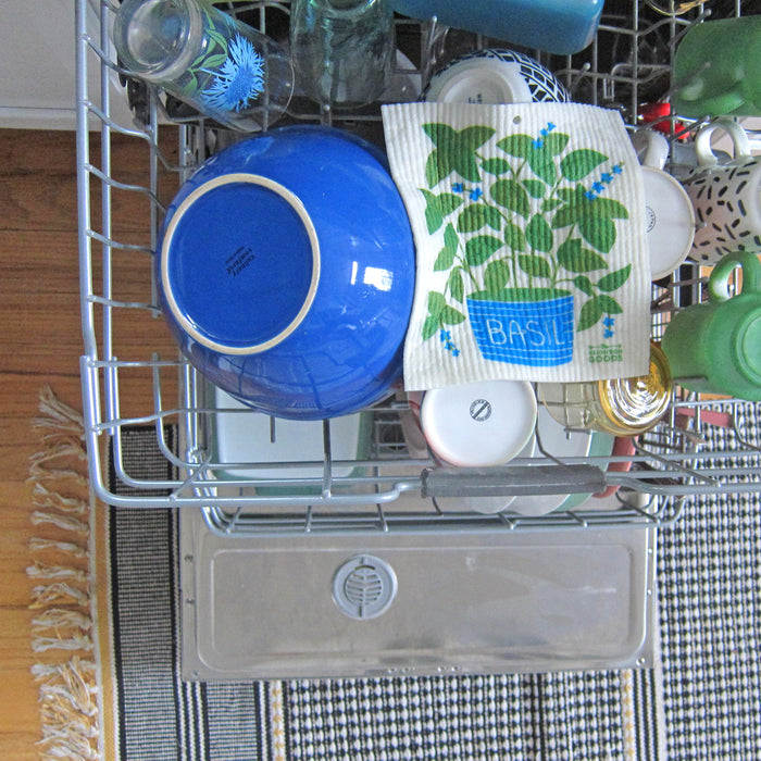 A basil sponge cloth placed on the top rack of a dishwasher ready to be cleaned.