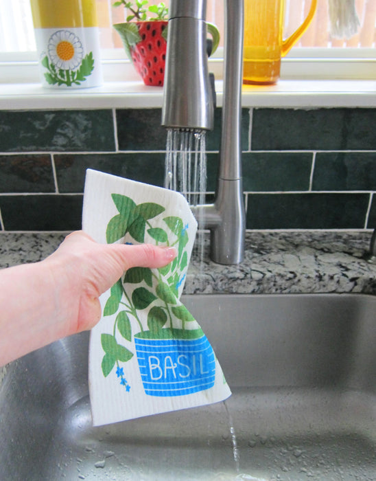 A basil sponge cloth is put under running water in a sink.