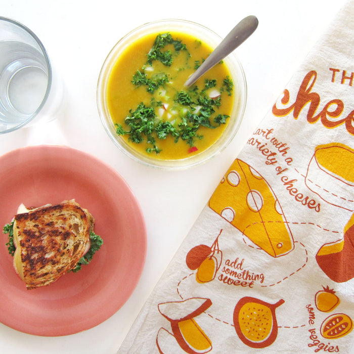 Cheese dish towel lying next to grilled cheese and soup