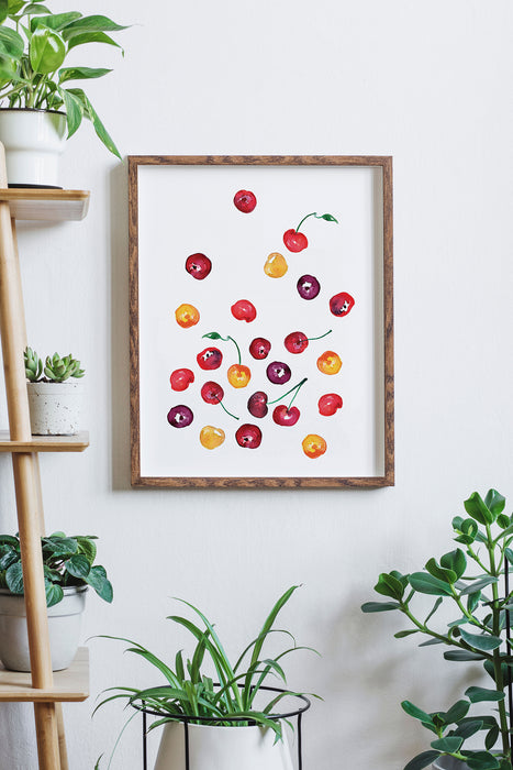 Watercolor cherries print framed amongst several houseplants