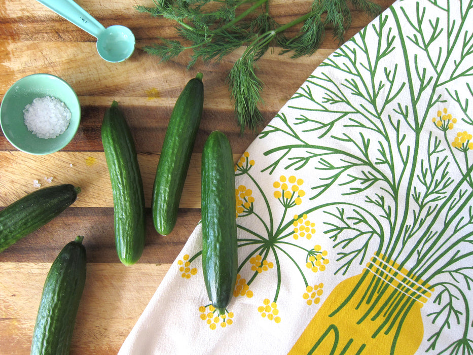 Dill dish towel, dill herb, and cucumbers on cutting board