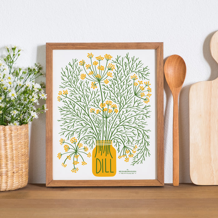 Dill print in small size framed alongside a wooden spoon, cutting board, and flowering plant