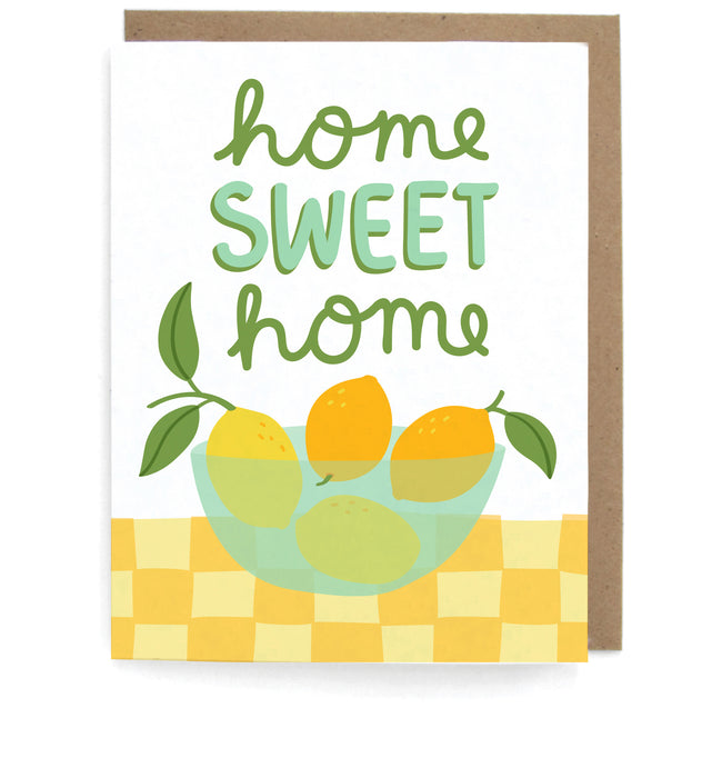 White card that pictures a bowl of lemons on a checkerboard table, featuring the phrase"Home sweet home," with a brown envelope