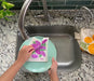 Lilac sponge cloth being used to clean dishes in a sink