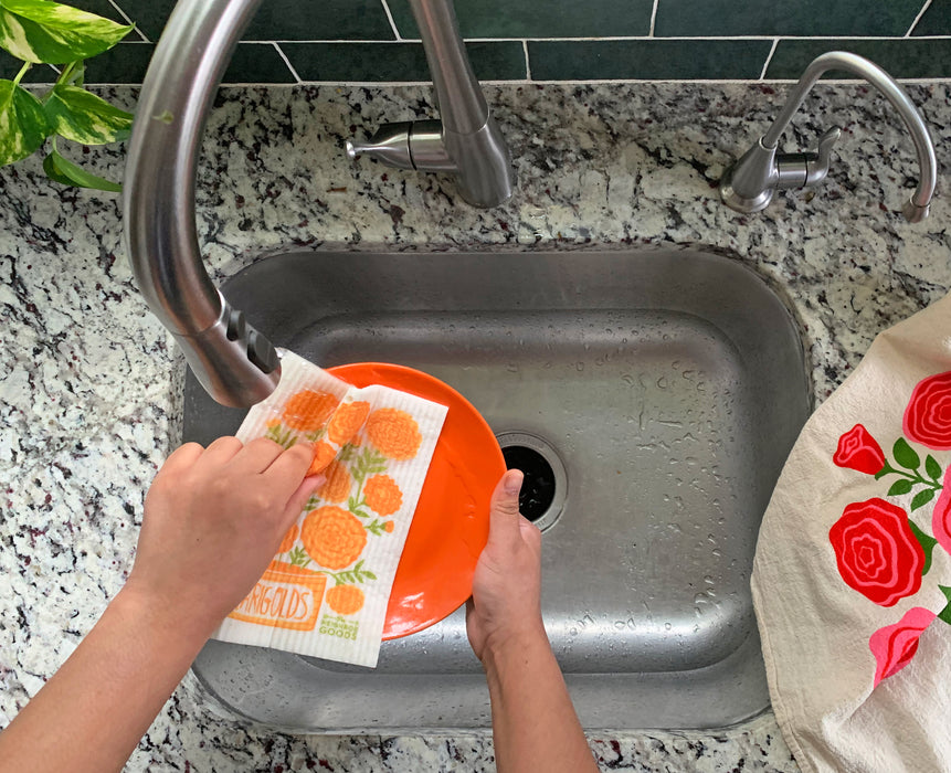 A woman washes a plate with a marigolds sponge cloth.