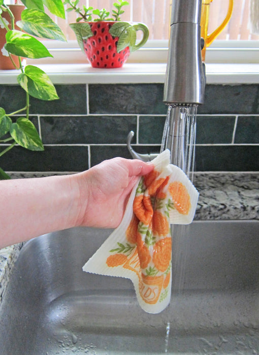 A marigold sponge cloth becomes wet under running water in a kitchen sink.