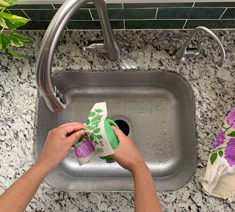 Mint sponge cloth being used to clean dishes in a sink