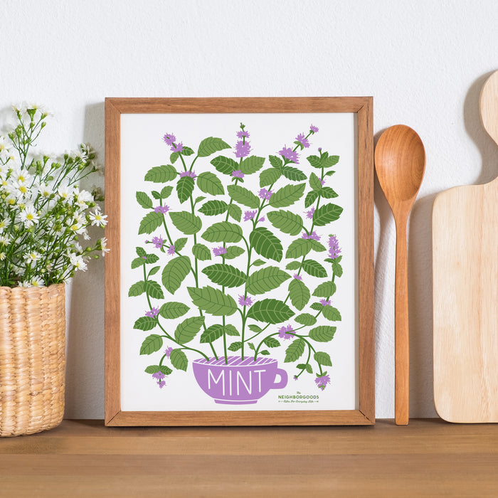 Mint print in small size framed alongside a wooden spoon, cutting board, and flowering plant