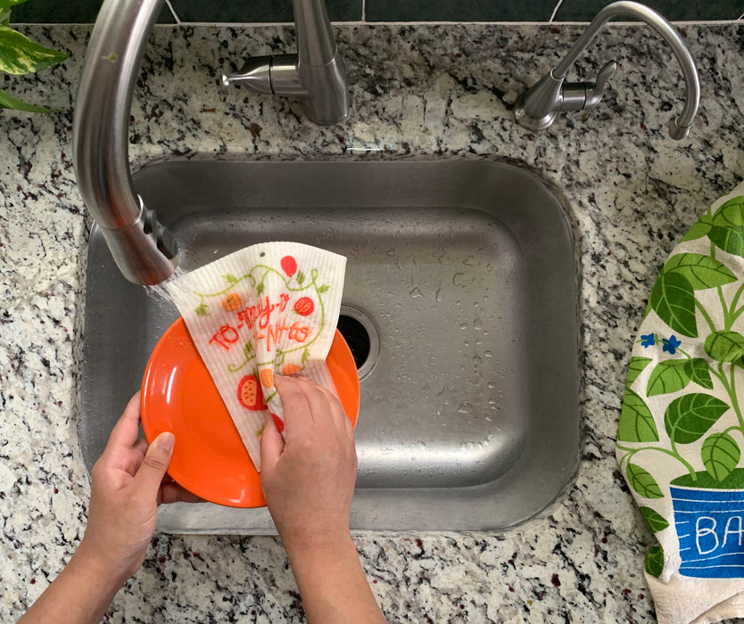 Tomato sponge cloth being used to clean dishes in a sink
