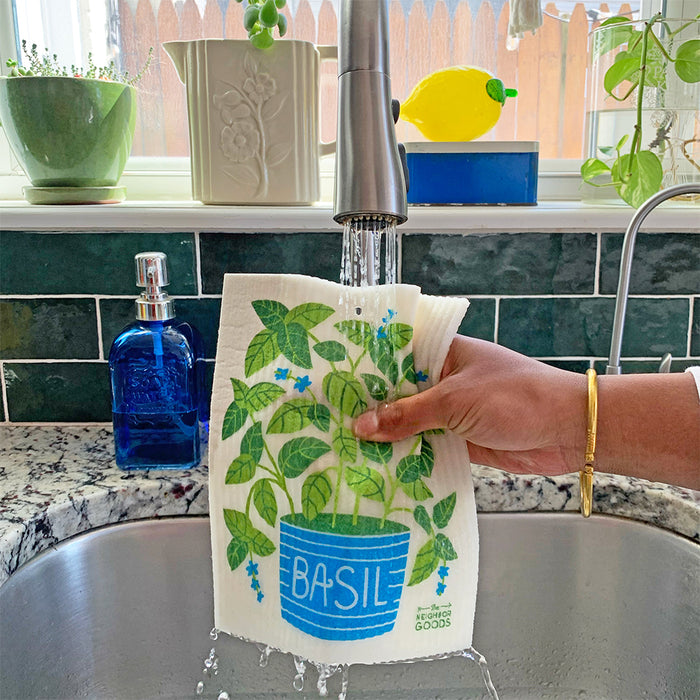 A basil sponge cloth becomes wet under the kitchen sink faucet.