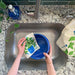 A woman washes a bowl with a basil sponge cloth.
