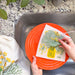 A woman washes a plate with a dill sponge cloth.