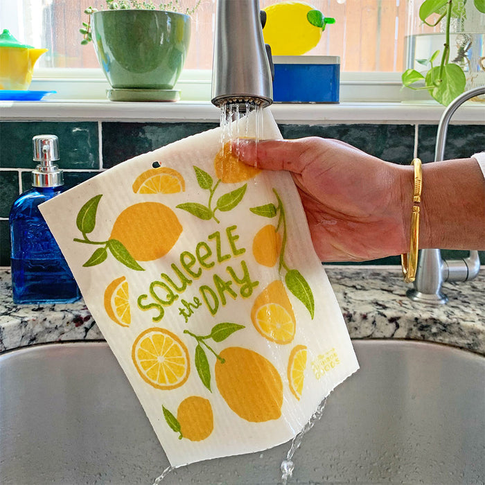 A lemon sponge cloth becomes wet under running kitchen faucet.