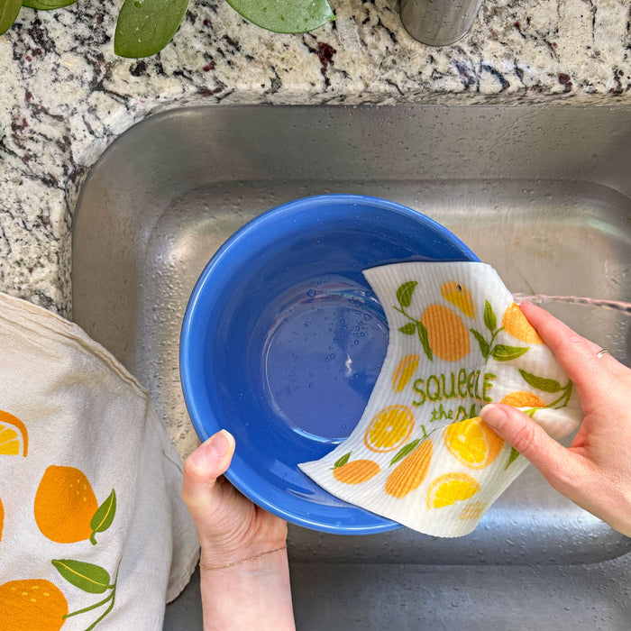 A woman washes a bowl with a lemon sponge cloth.