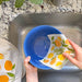 A woman washes a bowl with a lemon sponge cloth.
