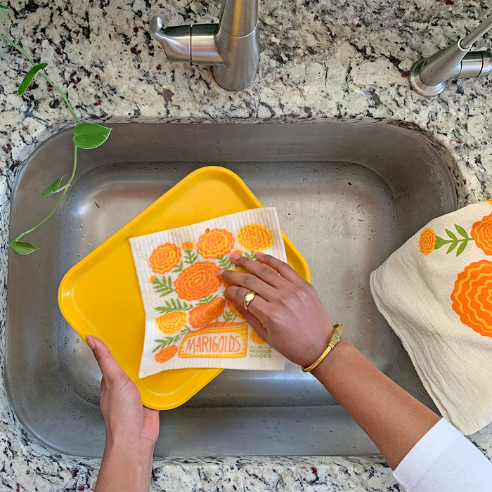 A woman washes a serving platter in the kitchen sink with the marigolds sponge cloth.