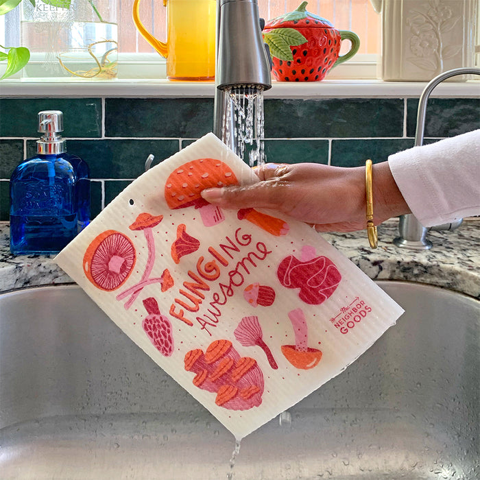 A mushroom sponge cloth becomes wet under the running kitchen sink faucet.