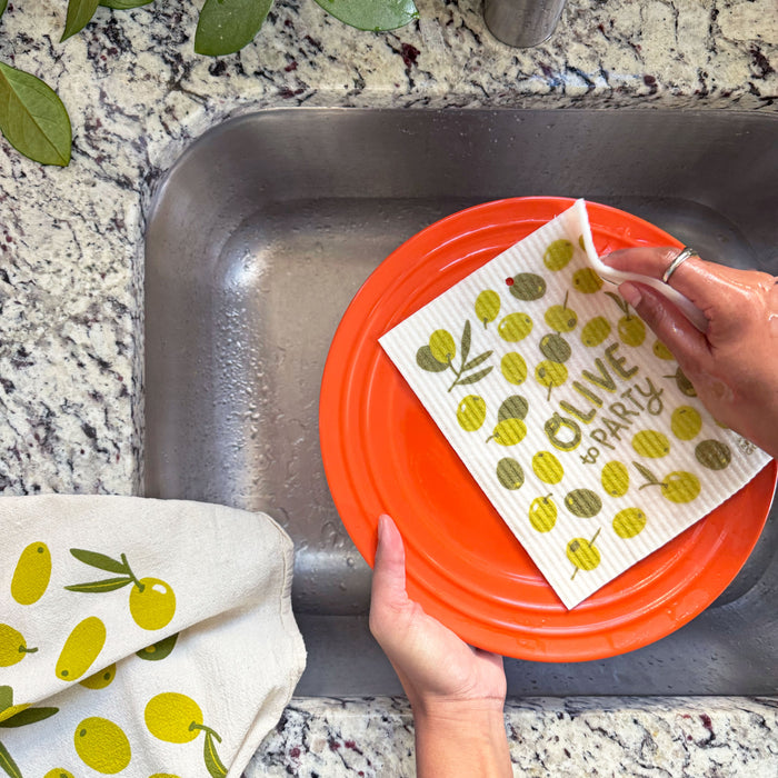 A woman washes a plate in the kitchen sink with an olive sponge cloth.