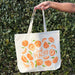 A woman holds a peach tote bag.