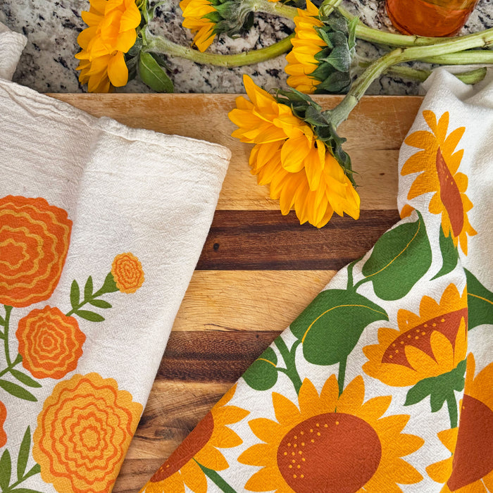 Sunflower and marigold dish towels lying next to each other on a cutting board.