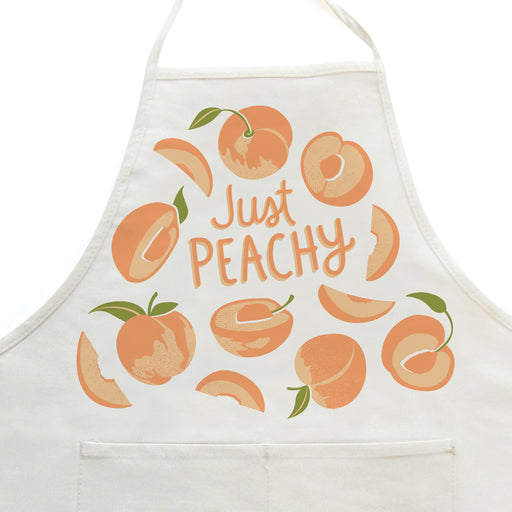 Close-up on white apron with peaches design, featuring the phrase "Just peachy"