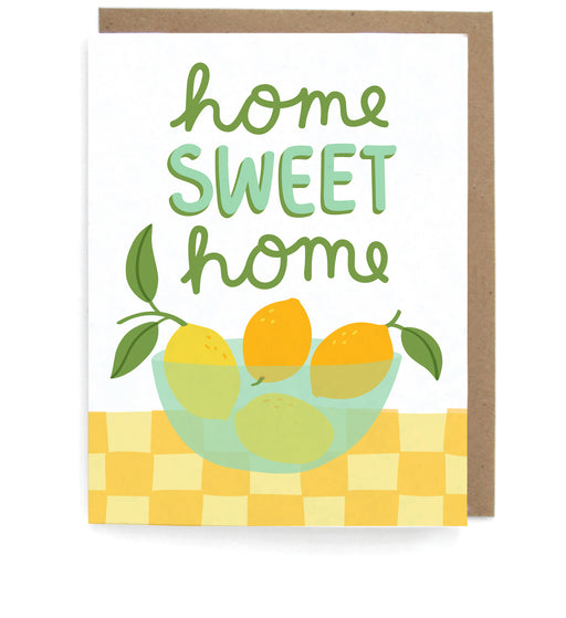 White card that pictures a bowl of lemons on a checkerboard table, featuring the phrase"Home sweet home," with a brown envelope